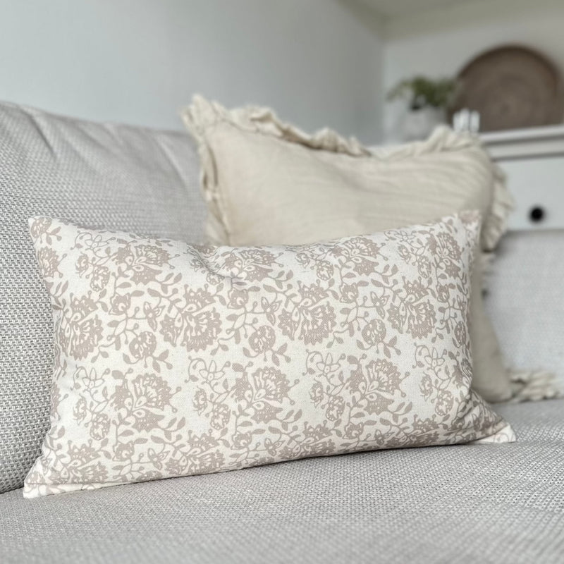 rectangle cream cushion with delicate beige floral details all over. Cushion sat on a cream sofa
