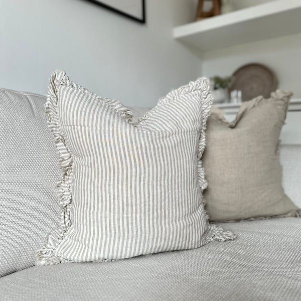 ruffled edge cream cushion with an vertical close repeating beige stripe. Sat on a cream sofa.