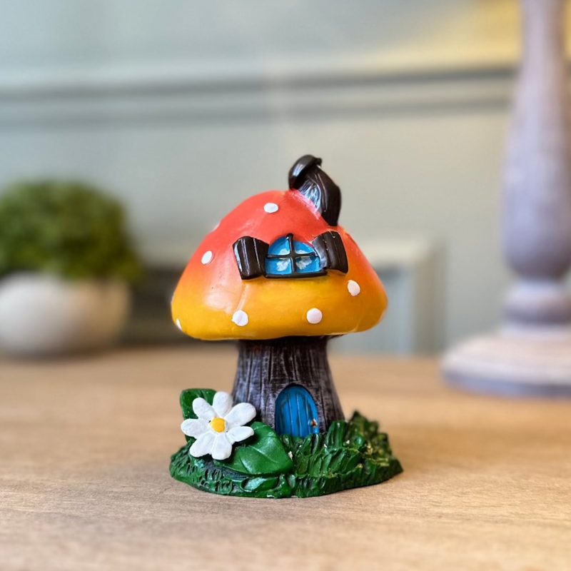 Ceramic toadstool incense burner. orange top with white polka dots. Base is like a tree trunk with a little blue door. Sat on a grassy base with a white daisy.