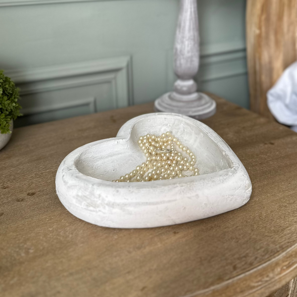 white stone love heart shape ornamental dish with jewellery stored inside on a wooden bedside table.