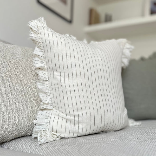 ruffled edge cream square cushion with an olive vertical pin stripe. Sat on a cream sofa.