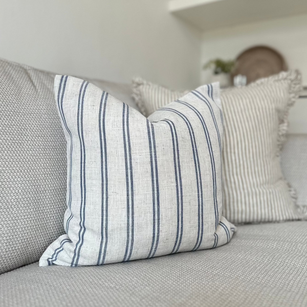 Light cream cushion with navy blue vertical double stripe motif all the way around the cushion. sat on a light cream sofa