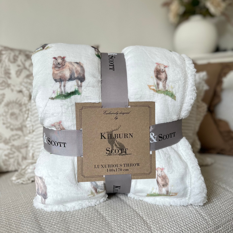Soft, fluffy White sherpa blanket with an all over white sheep print. Sat on a cream sofa