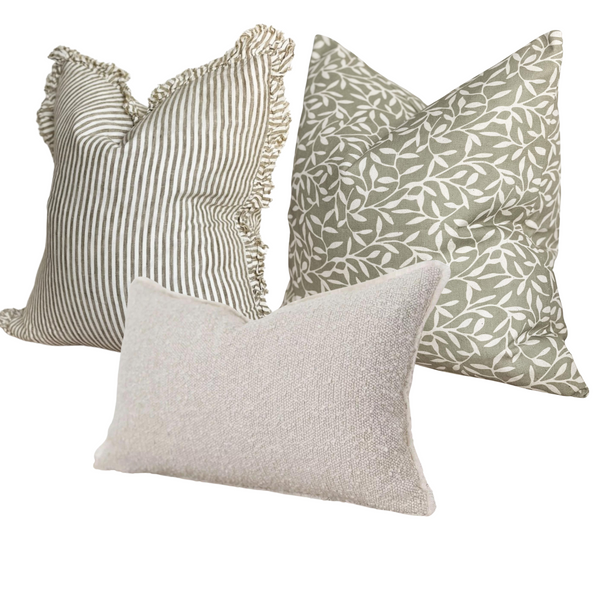 1 square ruffled edge linen cream and olive green vertical repeating stripe cushion. 1 square cotton olive green cushion with an all over cream olive leaf print. 1 rectangle cream boucle cushion. All sat on a plain white background for contrast.