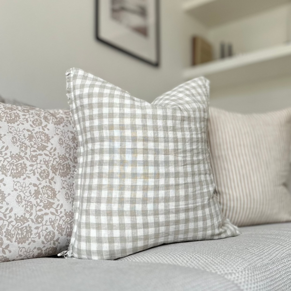 square weathered edge cream linen cushion with a beige gingham pattern, sitting on a cream sofa in a country inspired living room.