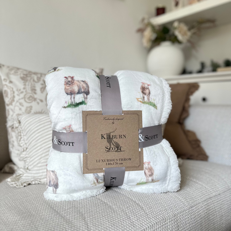 Soft, fluffy white sherpa blanket with an all over white sheep print. Sat on a cream sofa
