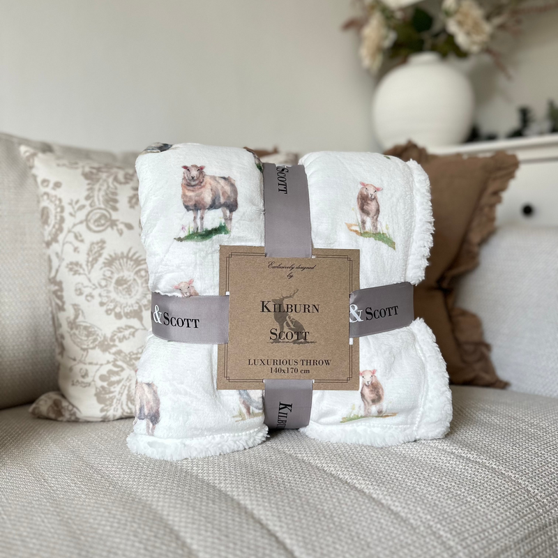 Soft, fluffy white sherpa blanket with an all over white sheep print. Sat on a cream sofa